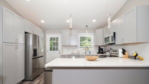 A modern kitchen with white cabinetry, stainless steel appliances, a large island, and pendant lighting. - Charming Cary Home~Centrally Located~Comfortable beds (Cary)