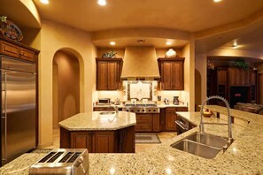 Una cocina con encimeras de granito, electrodomésticos de acero inoxidable, armarios de madera y una isla central con fregadero.