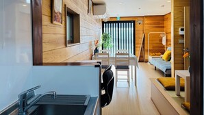 A modern hotel room with a kitchen area, a dining table, and a sofa.