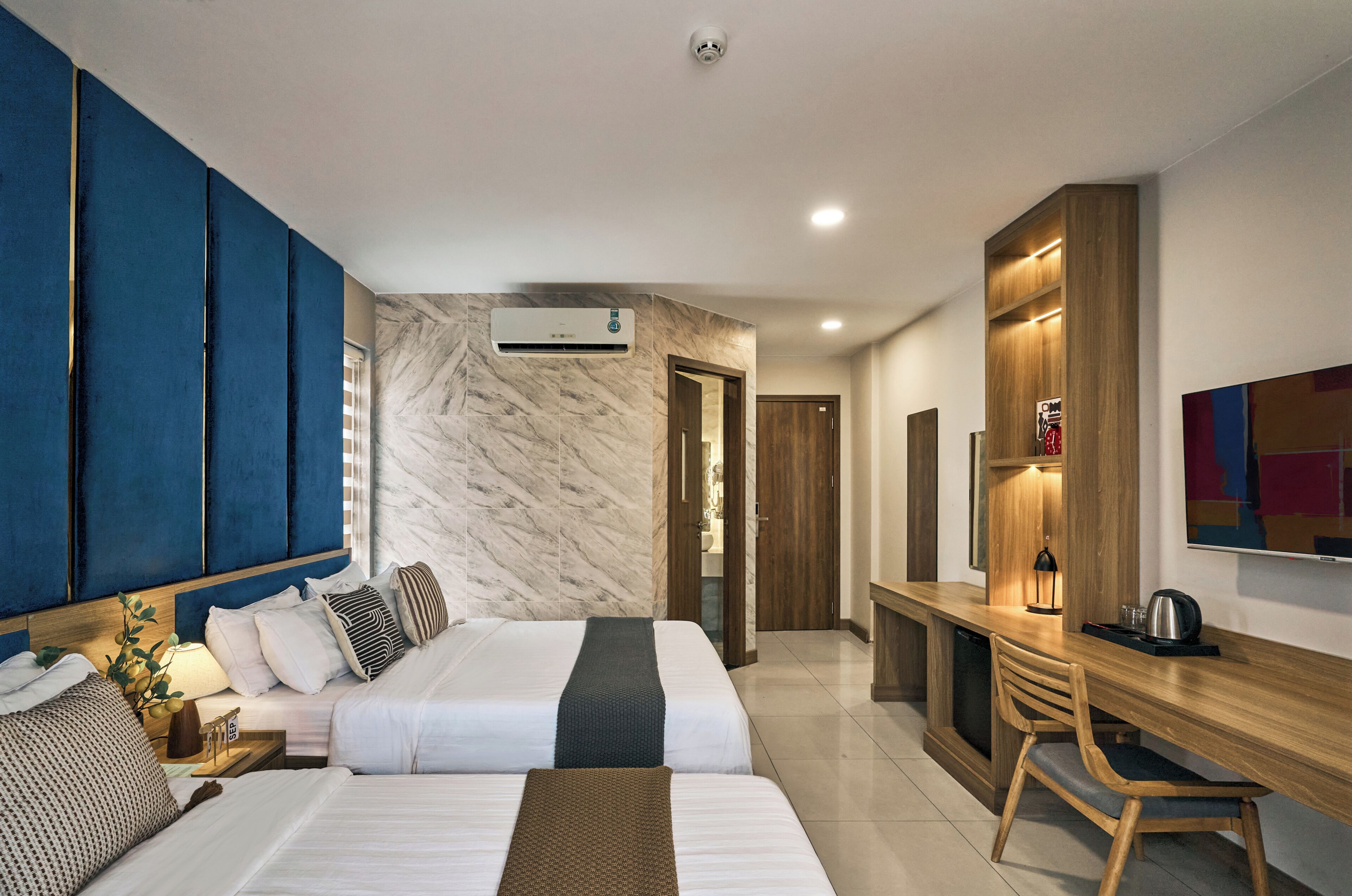 Una habitación de hotel con cama, mesita de noche, lámpara y un escritorio con silla.