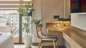 Habitación de hotel moderna con un escritorio de madera, una silla, una planta en maceta y vistas a la ciudad.