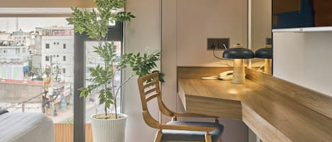 Une chambre d’hôtel moderne avec un bureau en bois, une chaise, une plante en pot et une vue sur la ville.