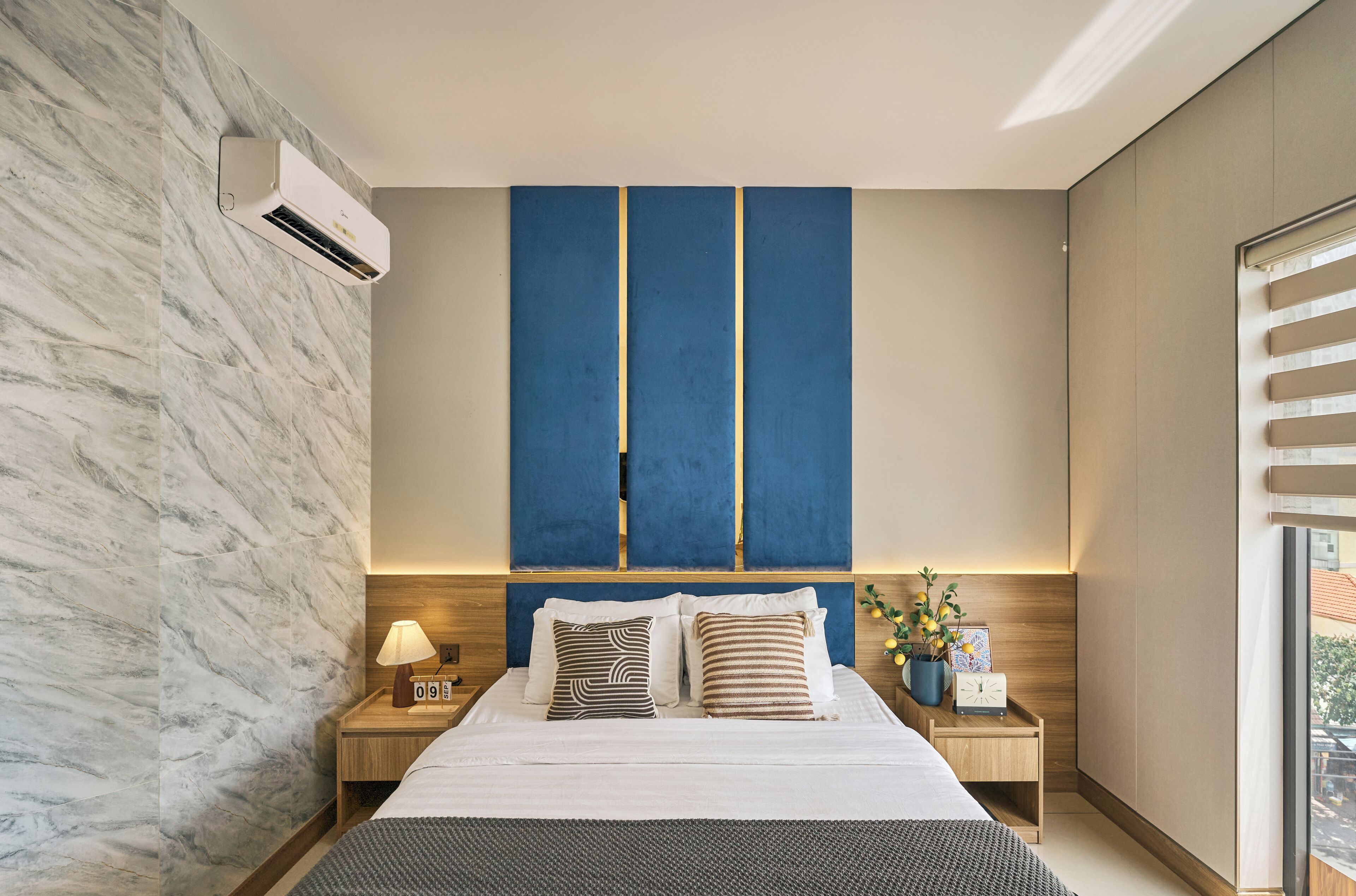 A modern bedroom with a bed, nightstands, a wall-mounted air conditioner, and a window with blinds.