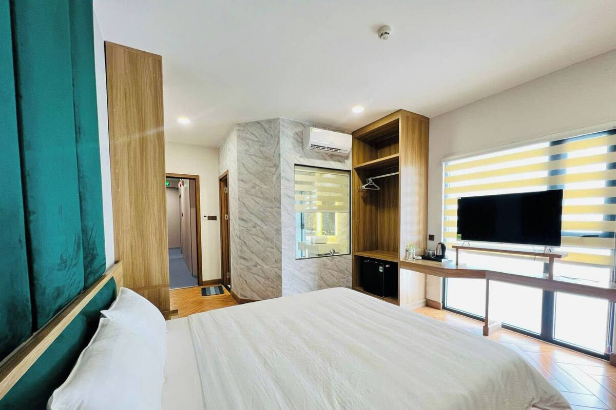 Habitación de hotel moderna con una cama grande, televisor, armario y baño visible a través de una puerta de vidrio.