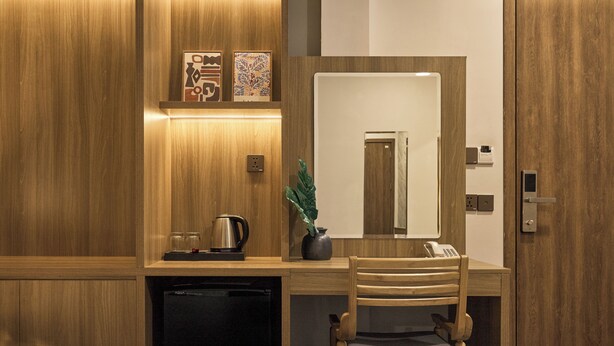 A hotel room with a wooden desk, a bed with a green blanket, a potted plant, a mirror, and a telephone. - Tran Long District 12 (Ho Chi Minh City)