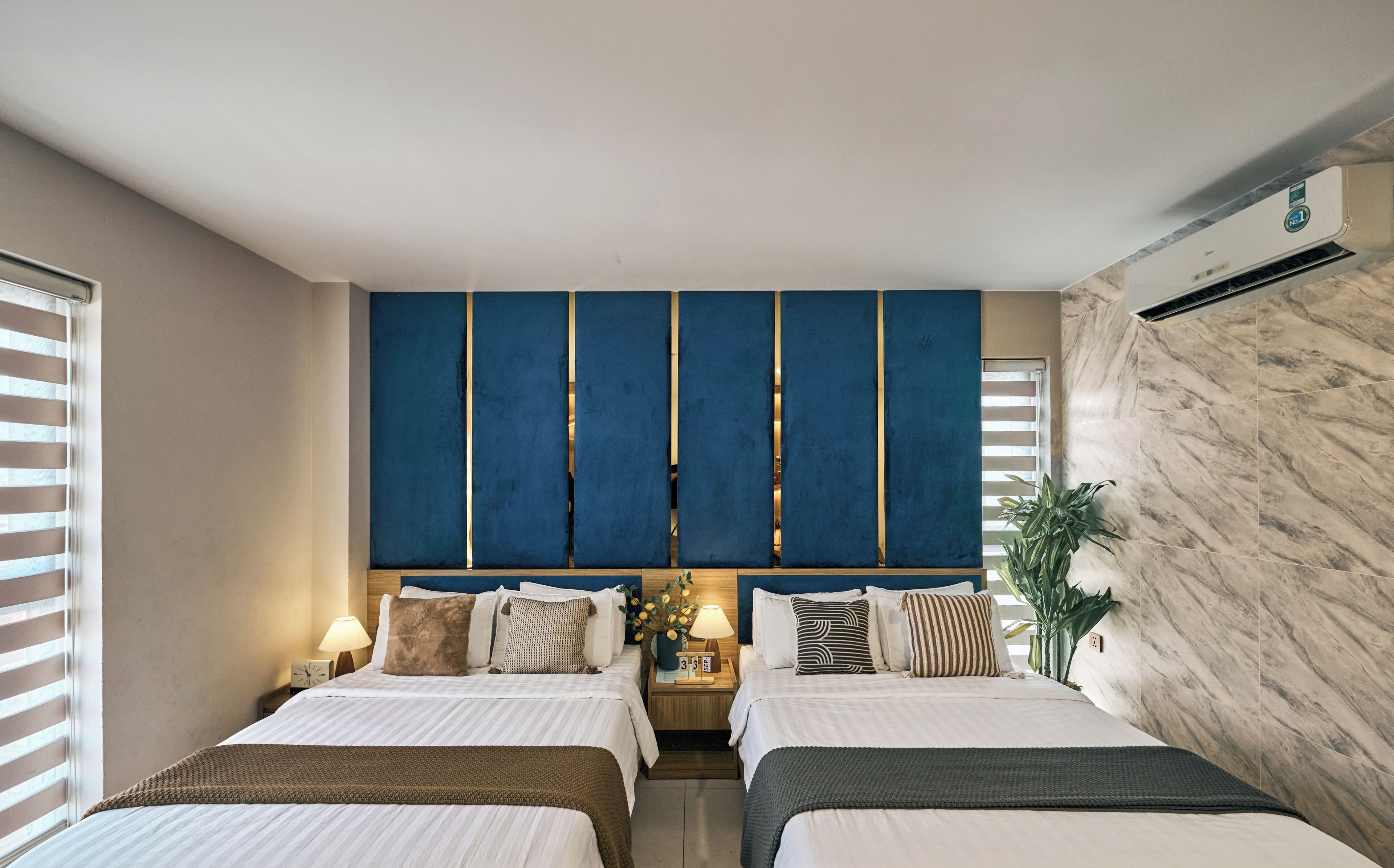 A hotel room with two beds, a large blue cabinet, a marble wall, and a potted plant.
