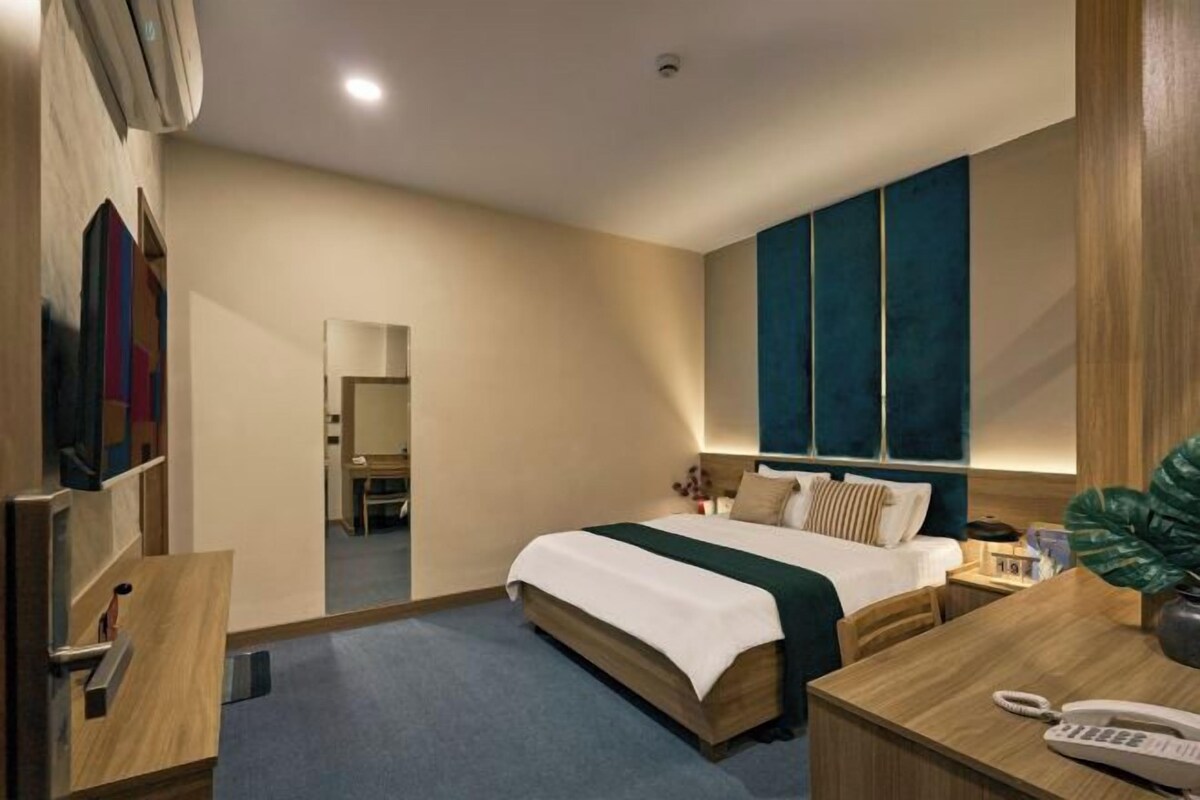 Una habitación de hotel con cama, mesita de noche, lámpara y espejo.