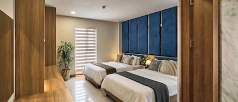 Une chambre d’hôtel avec deux lits, une grande fenêtre avec des stores, une plante en pot et un mur d’accent bleu.