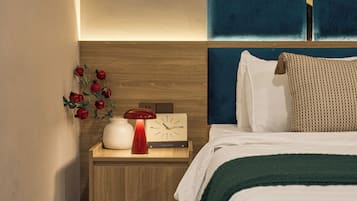 A neatly made bed with a green blanket, a bedside table with a red lamp, and a wall-mounted clock.