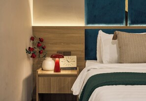 Ein ordentlich bezogenes Bett mit einer grünen Decke, ein Nachttisch mit einer roten Lampe und eine an der Wand befestigte Uhr.