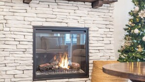 A stone fireplace with a glass front, a Christmas tree, and a round wooden table.