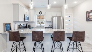 A modern kitchen with white cabinets, a stainless steel refrigerator, a granite countertop, and three bar stools.