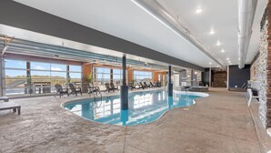 An indoor swimming pool with lounge chairs and a view of the outdoors.