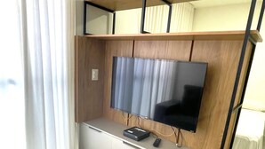 Un salon moderne avec un téléviseur à écran plat fixé à un meuble mural en bois, une télécommande et un petit appareil électronique posé sur le comptoir.