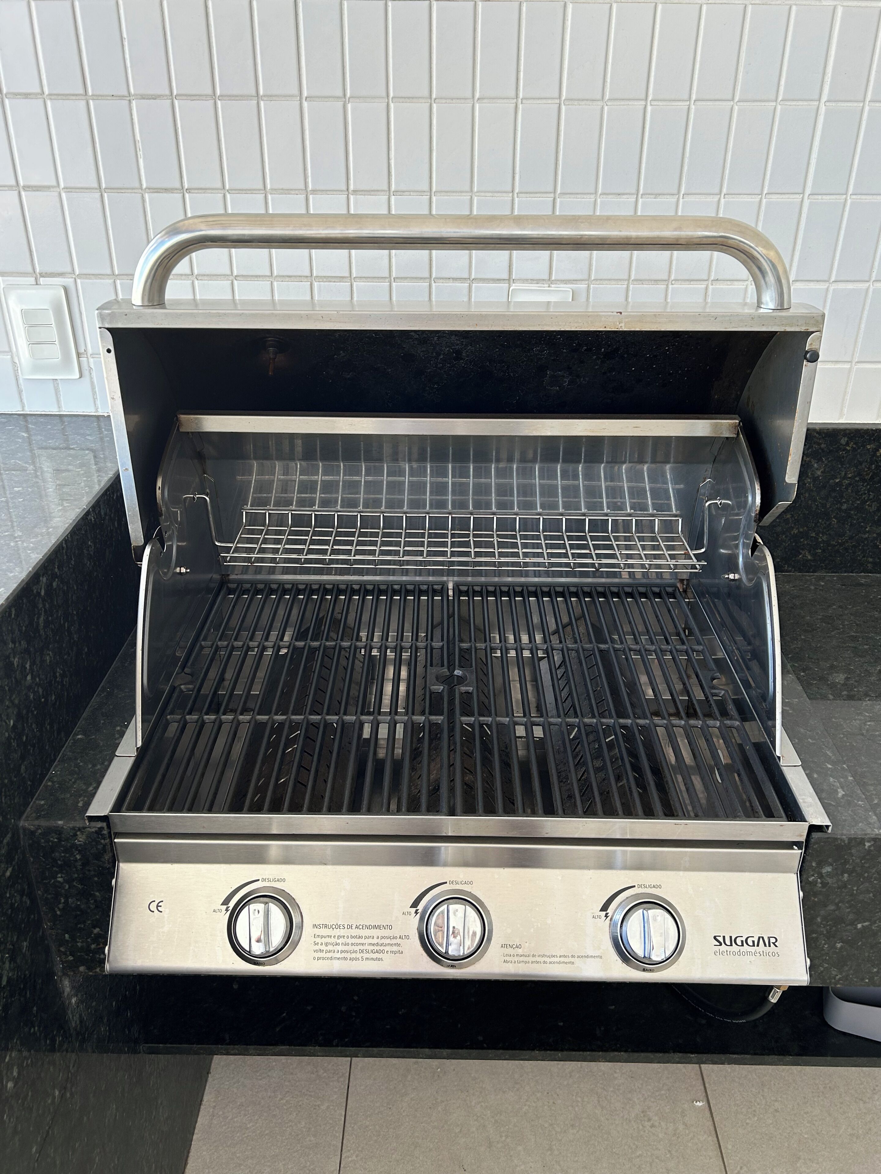 An open electric grill with a black cooking surface and stainless steel sides, placed on a dark countertop.
