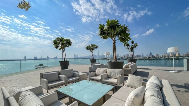 A rooftop terrace with outdoor seating, two potted trees, and a view of the city skyline across the water.