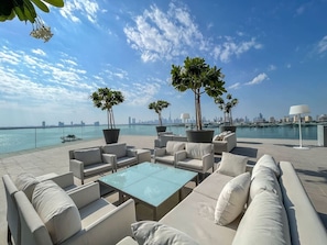 A rooftop terrace with outdoor seating, two potted trees, and a view of the city skyline across the water.