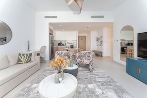 Una sala de estar moderna con un sofá, una mesa de centro y sillas, que da paso a una zona de cocina con una mesa de comedor.
