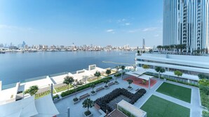 A modern high-rise building with a waterfront view, featuring a spacious outdoor area with seating and greenery.