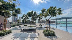 A rooftop pool area with lounge chairs, a seating area, and palm trees.