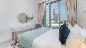 A modern bedroom with a large bed, a bedside table, a mirror, and a view of a cityscape through large windows.
