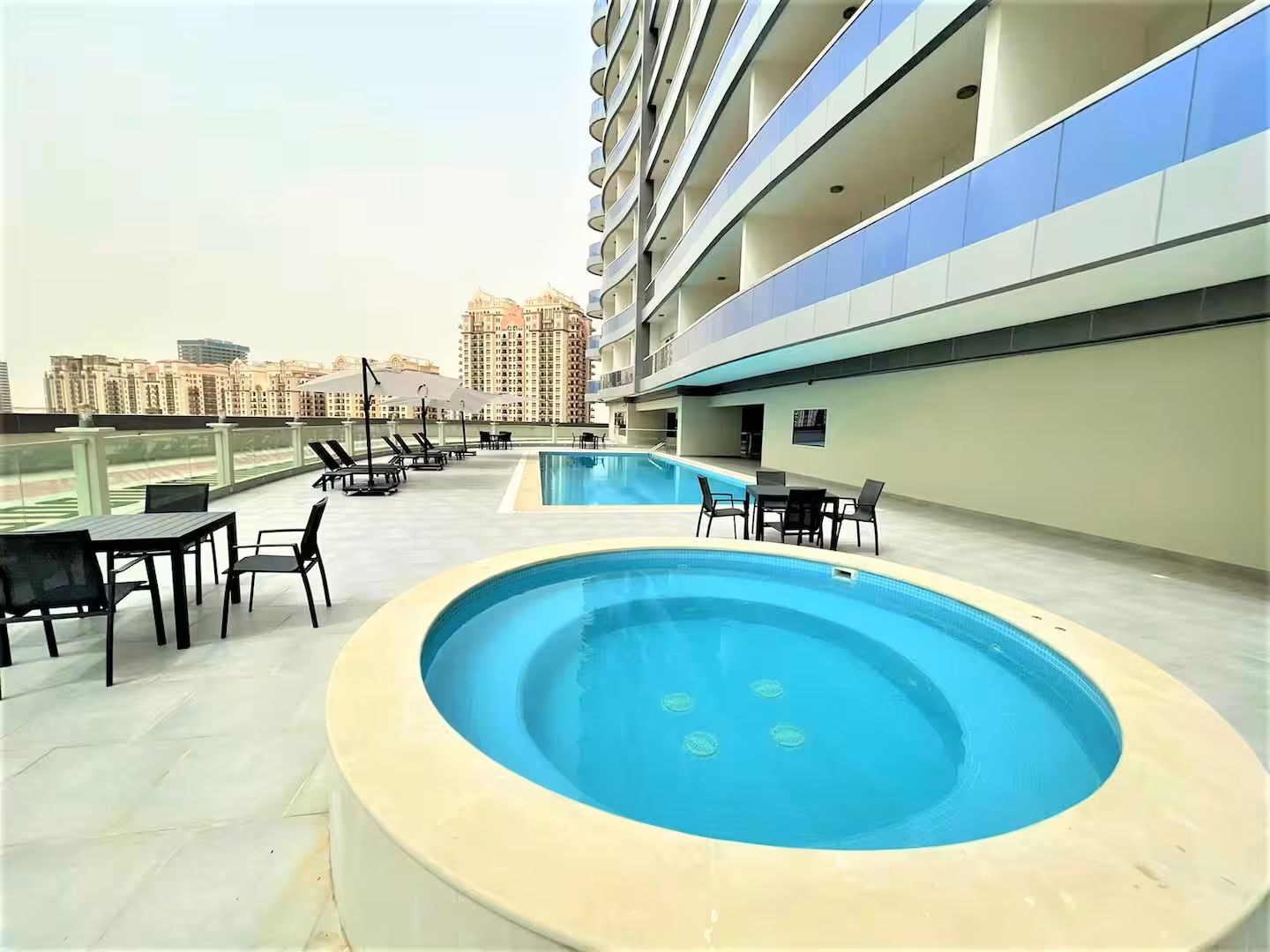Un espace piscine aménagé sur le toit, avec des chaises longues et des tables, entouré de gratte-ciel.