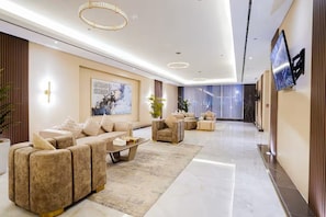 A modern hotel lobby with a sofa set, a coffee table, and a television on the wall.