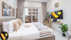 A modern bedroom with a bed, a TV, a desk, and a balcony.