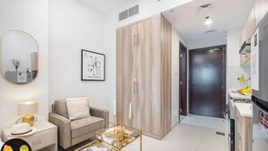 A modern living room with a sofa, a coffee table, and a side table with a lamp. There is a wardrobe with a mirror and a framed picture on the wall.