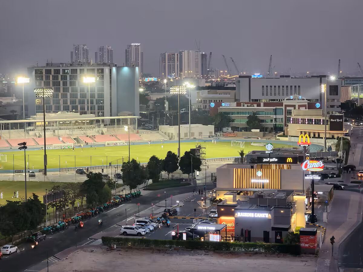Ein Stadion mit einem Fußballplatz, umgeben von modernen Gebäuden und einem Parkplatz.