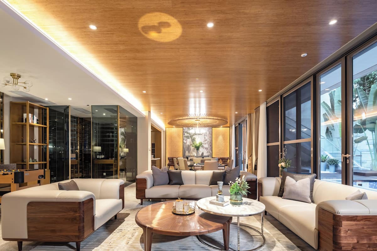 Una sala de estar moderna con techo de madera, ventanas grandes y un área central de estar con una mesa de centro.