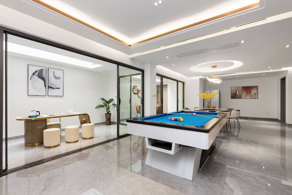Un área moderna con mesa de billar en interior, separada por un vidrio, con mesa de billar y zona de estar con una pequeña mesa y sillas.