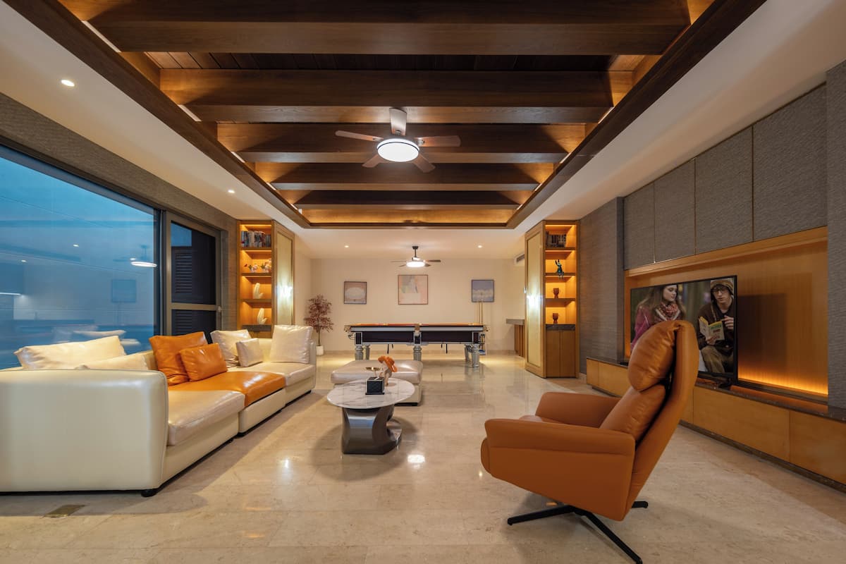 Una sala de estar moderna con un sofá, un sillón y una mesa de centro. Hay un ventilador de techo, iluminación empotrada y un ventanal grande.