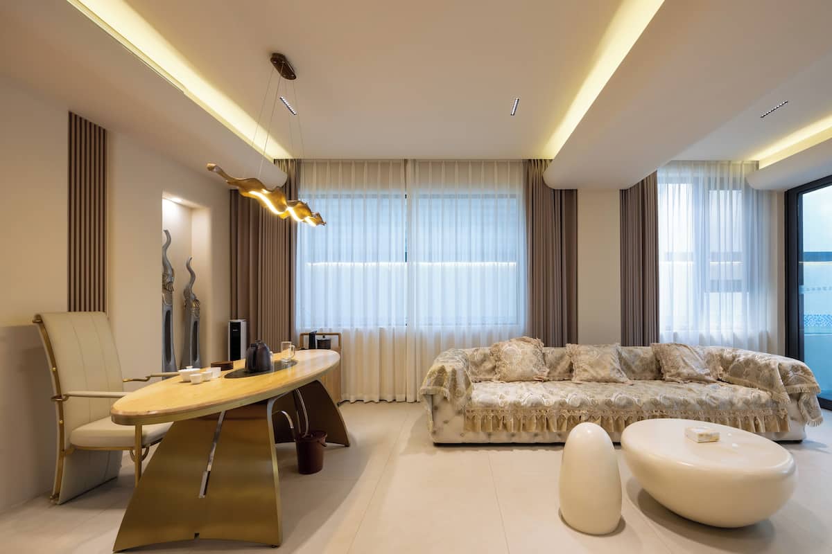 Una sala de estar moderna con un sofá, una mesa de centro y una silla. Hay una ventana con cortinas y una lámpara en el techo.