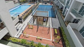 Zona de piscina en la azotea con cancha de tenis, equipo de ejercicios y sillas de descanso.
