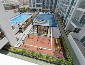 Een zwembad op het dak met een tennisbaan, fitnessapparatuur en ligbedden.