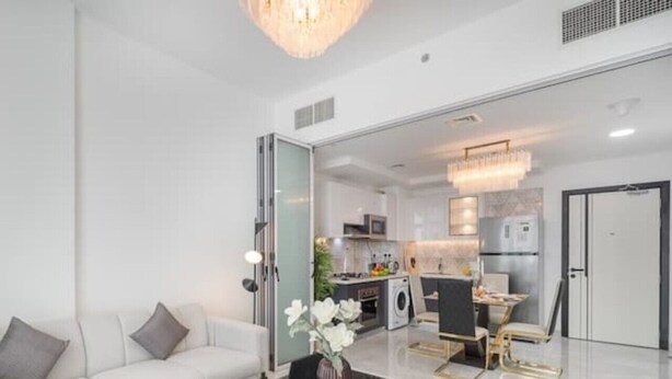 Una sala de estar moderna con un sofá blanco, una mesa de centro con un florero y un comedor con mesa y sillas.