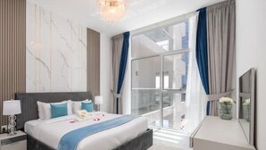 Habitación de hotel moderna con una cama grande, una mesita de noche con lámpara, un aparador y un ventanal con cortinas.
