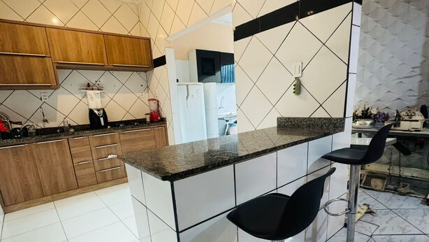 Cozinha moderna com área de bar, armários de madeira, painel de azulejos branco e preto e um banquinho de aço inoxidável.
