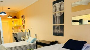 Quarto de hotel com duas camas, uma escrivaninha, uma cadeira, um espelho e obras de arte na parede.