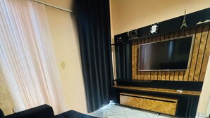 Sala de estar com sofá preto, televisão de tela plana presa a uma parede de madeira e uma pequena decoração da Torre Eiffel.