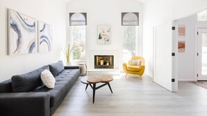 Un salon spacieux avec une cheminée, un canapé, un fauteuil jaune et des œuvres d’art abstraites accrochées aux murs.