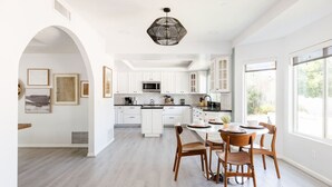 Une cuisine moderne avec des meubles blancs, un îlot central et un coin repas doté de chaises en bois.
