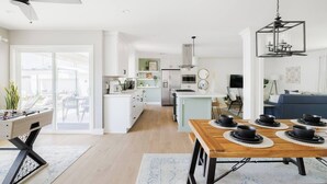 A modern kitchen with white cabinets, a central island, and a dining area with a wooden table and chairs.