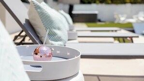 A sun lounger with a white cushion, a striped pillow, and a decorative object on a table.