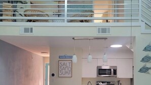 Een modern appartement met een vide en slaapkamer, een keuken met een centraal eiland, en een eethoek met uitzicht op het strand.