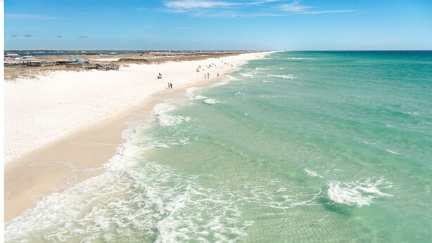 Een strand met helder turquoise water, een zandstrand en een pier op de achtergrond.
