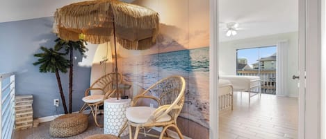 Une pièce décorée d’une fresque représentant une plage, meublée de meubles en osier et offrant une vue sur l’extérieur.