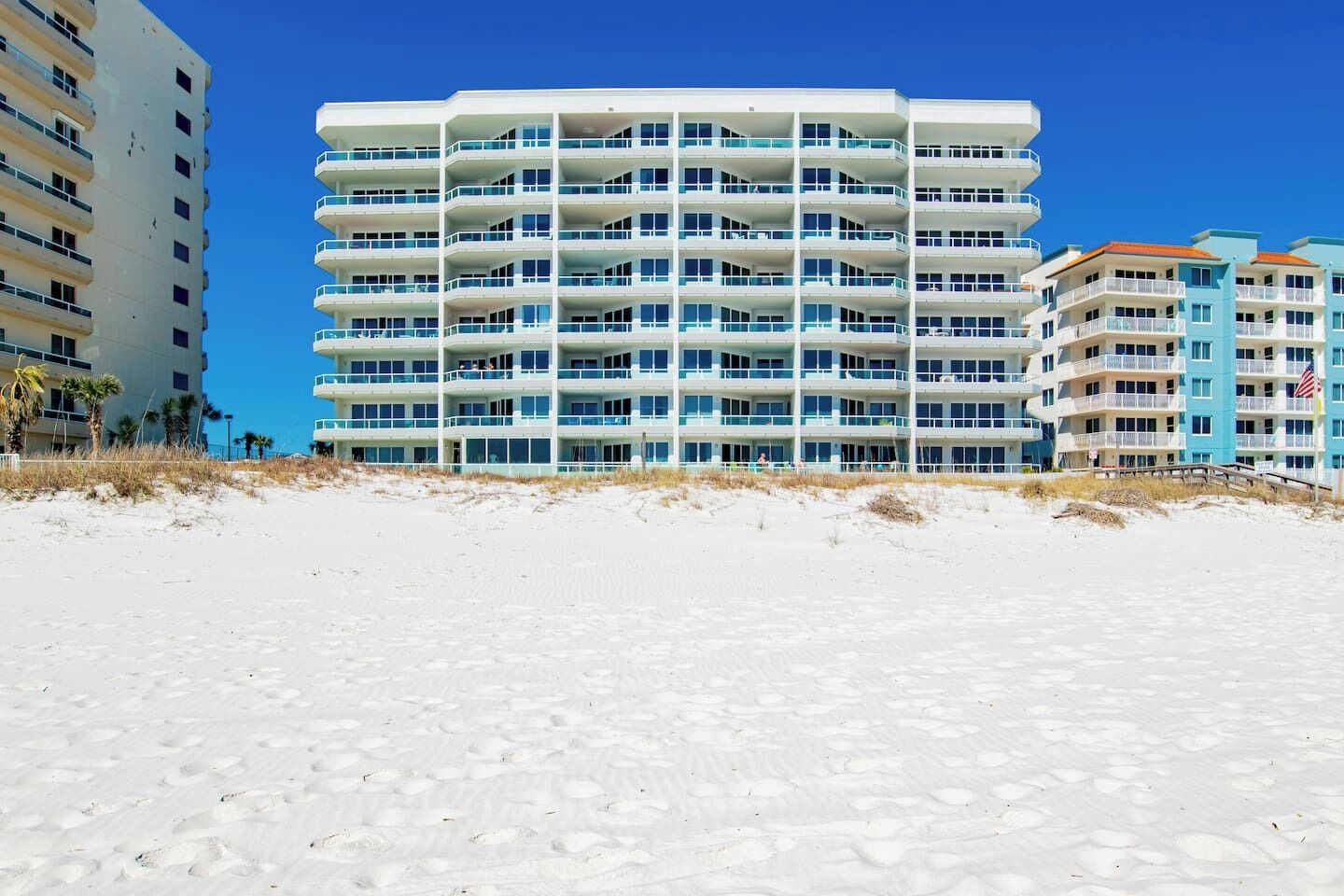 A multi-story hotel with balconies, located on a sandy beach.
