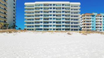 A multi-story hotel with balconies, located on a sandy beach.